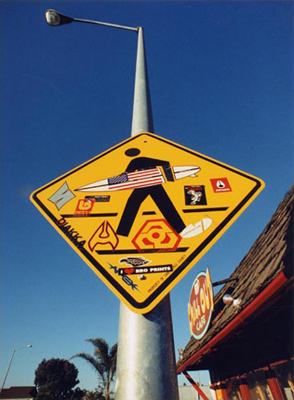 lit fuze surfer pedestrian crossing sign against blue sky created by Daniel Billotte and Matthew Flansburg in Santa Cruz California 2001 viral vandalism project to improve city signs with appropriate surf branding out side Chill Out Cafe East Cliff fLANSBURG dESIGN